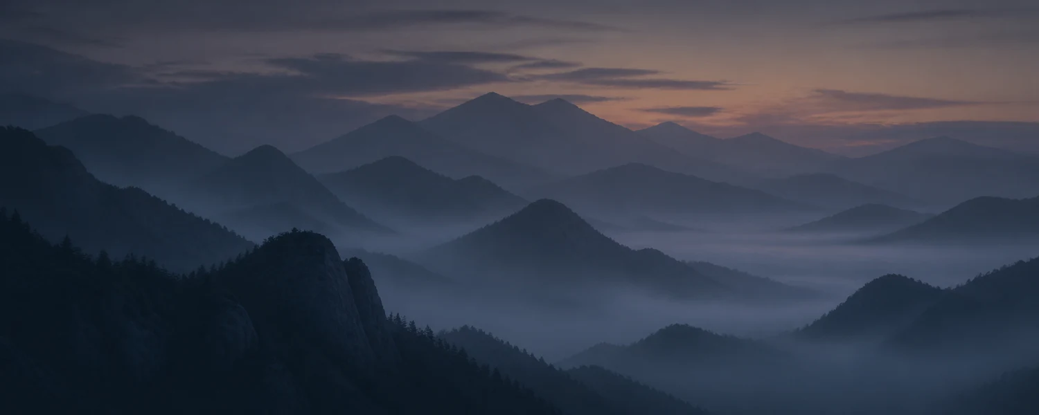 Layered misty mountain silhouettes at dusk in blue-gray fog